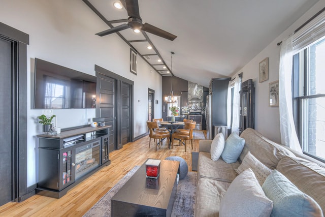 living area with a wealth of natural light, ceiling fan with notable chandelier, high vaulted ceiling, and light wood-style flooring