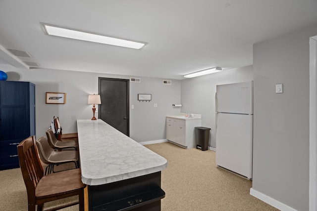 kitchen featuring baseboards, visible vents, freestanding refrigerator, a sink, and light countertops