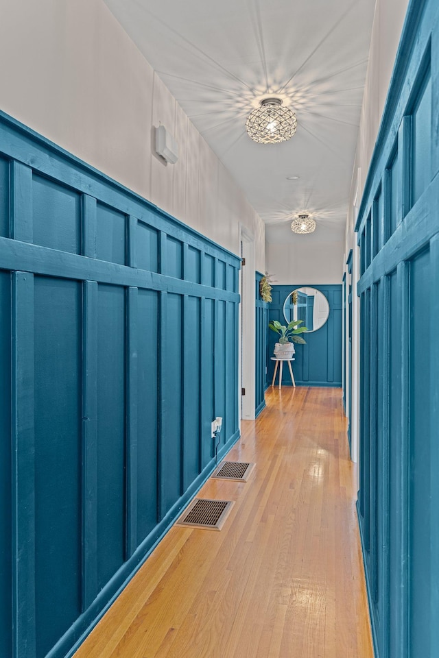 corridor with hardwood / wood-style flooring, a decorative wall, and visible vents