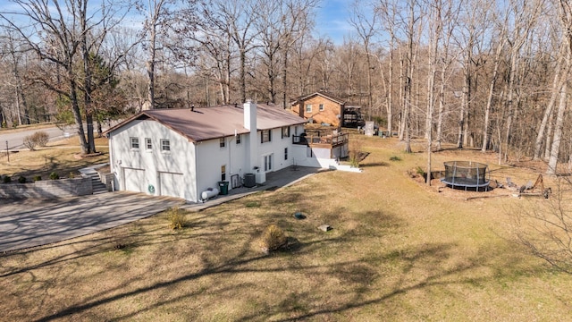 view of home's exterior featuring a trampoline, a lawn, a chimney, driveway, and an attached garage