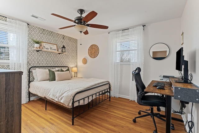 bedroom with a ceiling fan, visible vents, baseboards, light wood-style floors, and an accent wall