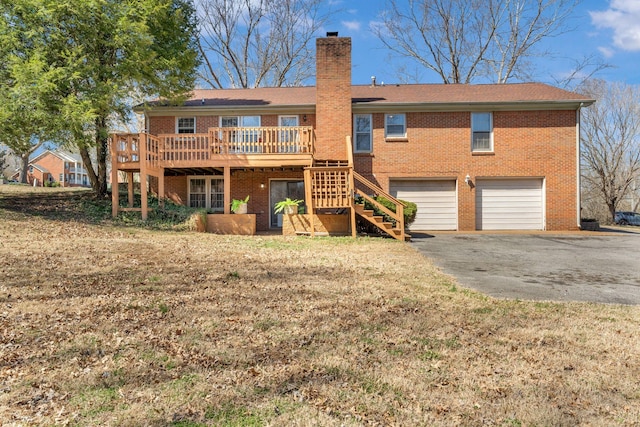 rear view of property with aphalt driveway, stairway, an attached garage, brick siding, and a chimney