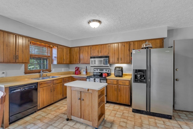 kitchen featuring light floors, a sink, light countertops, appliances with stainless steel finishes, and brown cabinets