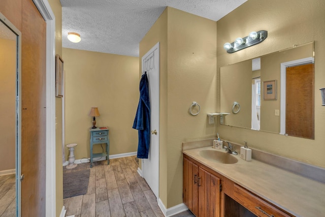 bathroom featuring baseboards, a textured ceiling, wood finished floors, and vanity