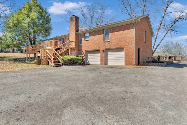 back of property featuring stairway, driveway, a chimney, a garage, and brick siding