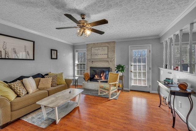 living area with a ceiling fan, crown molding, a brick fireplace, and wood finished floors