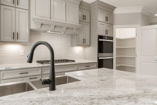 kitchen with tasteful backsplash, crown molding, light stone countertops, double oven, and a sink