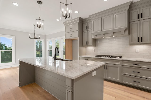 kitchen with stainless steel gas cooktop, gray cabinets, ornamental molding, a sink, and a chandelier