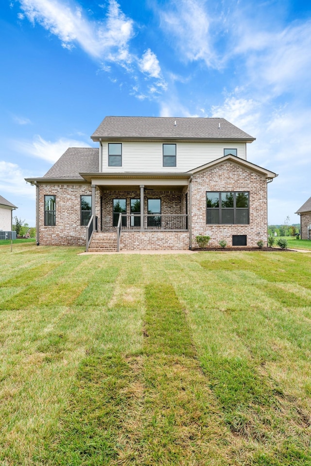 back of house featuring brick siding, covered porch, a lawn, and a shingled roof