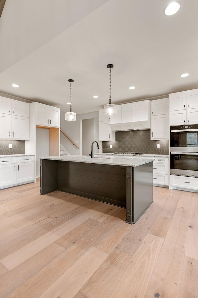 kitchen featuring light wood-type flooring, pendant lighting, a sink, double oven, and white cabinets