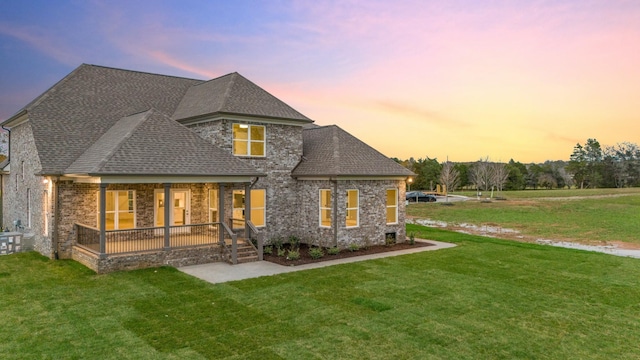 back of property featuring a lawn, covered porch, brick siding, and a shingled roof