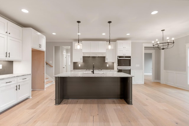 kitchen with crown molding, light wood-style flooring, stainless steel double oven, white cabinets, and a sink