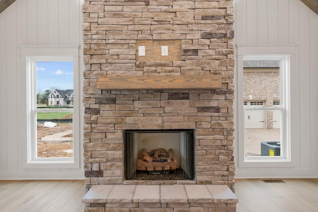 details with visible vents, central air condition unit, a stone fireplace, and wood finished floors