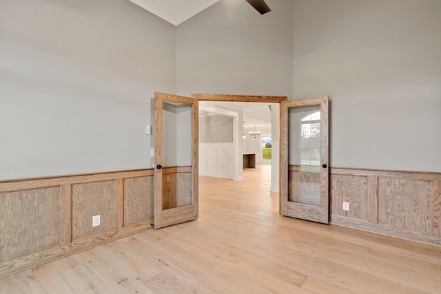 spare room featuring a high ceiling, a notable chandelier, light wood-style floors, and a wainscoted wall