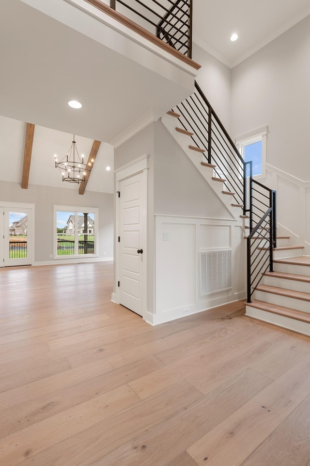 stairs with visible vents, beamed ceiling, wood finished floors, an inviting chandelier, and a decorative wall