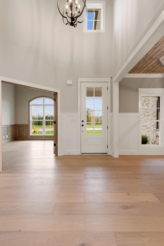 foyer featuring an inviting chandelier, hardwood / wood-style flooring, a wainscoted wall, and a towering ceiling