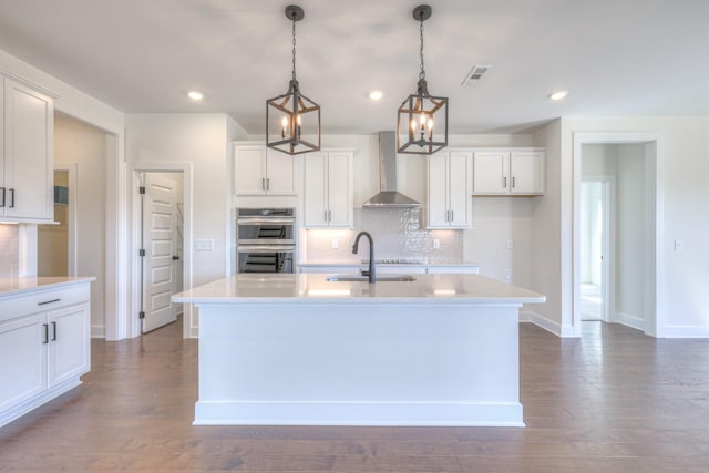 kitchen featuring visible vents, a sink, stainless steel double oven, wall chimney exhaust hood, and light countertops