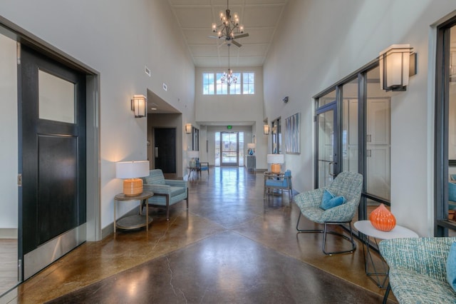 hallway with a high ceiling, baseboards, concrete floors, and an inviting chandelier