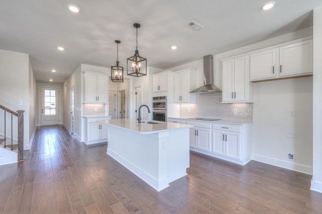 kitchen featuring a sink, dark wood-type flooring, light countertops, double oven, and wall chimney range hood