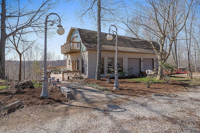 exterior space featuring a gambrel roof, roof with shingles, a garage, a balcony, and driveway