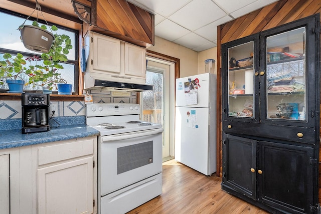 kitchen featuring under cabinet range hood, a drop ceiling, white appliances, light wood-style floors, and white cabinets