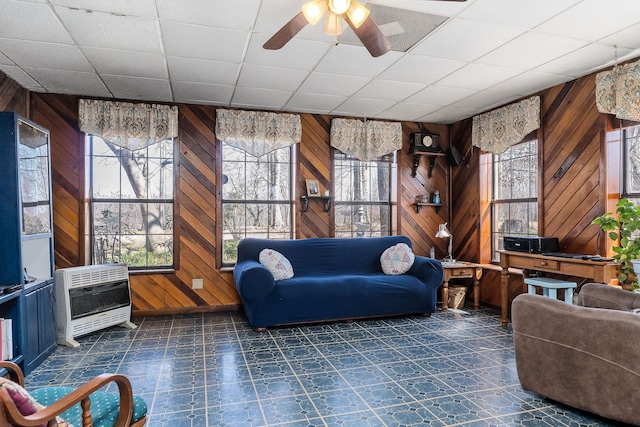 living area with ceiling fan, heating unit, wood walls, and dark floors