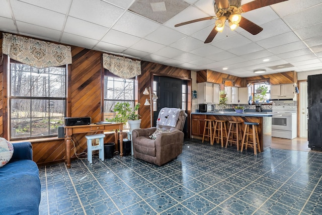 living area with a paneled ceiling, dark floors, wood walls, and ceiling fan