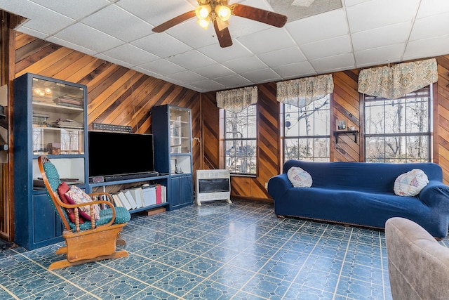 living area featuring heating unit, plenty of natural light, wood walls, and a ceiling fan