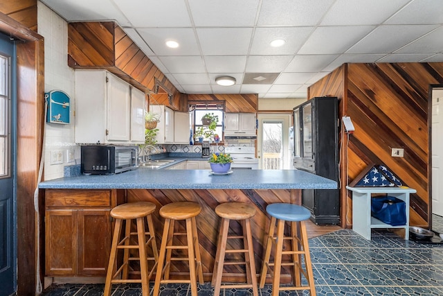 kitchen featuring under cabinet range hood, wood walls, a peninsula, electric stove, and a sink