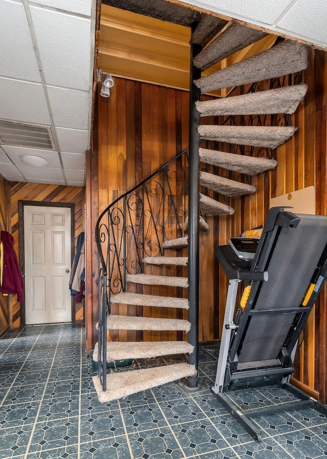 staircase with a drop ceiling, visible vents, and wood walls