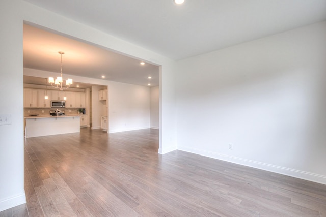 unfurnished living room with recessed lighting, wood finished floors, baseboards, and a chandelier