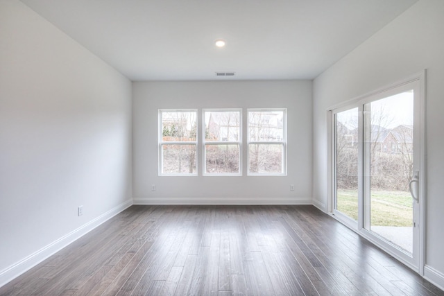 spare room with a wealth of natural light, visible vents, baseboards, and dark wood finished floors