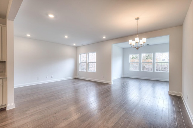 unfurnished living room with recessed lighting, baseboards, dark wood-type flooring, and an inviting chandelier