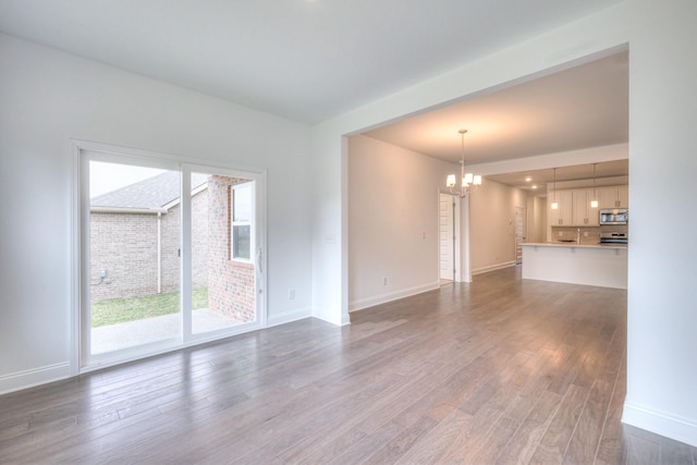 unfurnished living room with baseboards, an inviting chandelier, and wood finished floors