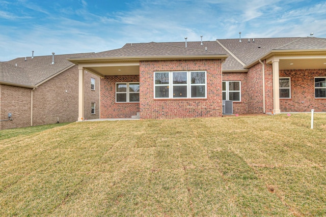 rear view of property with brick siding, central air condition unit, a lawn, and a shingled roof