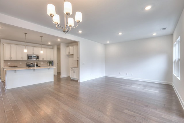 unfurnished living room with visible vents, a notable chandelier, wood finished floors, recessed lighting, and baseboards