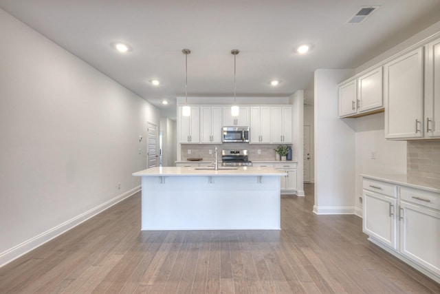 kitchen with a sink, wood finished floors, white cabinetry, stainless steel appliances, and light countertops