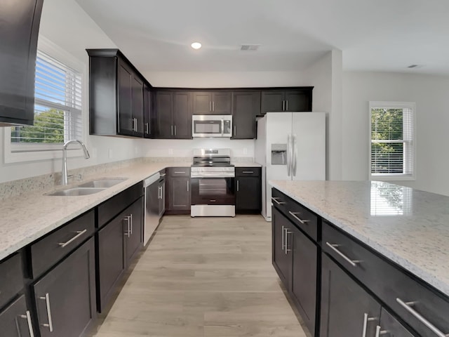 kitchen featuring visible vents, light stone countertops, light wood-style floors, stainless steel appliances, and a sink