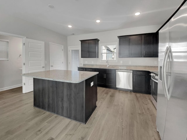 kitchen featuring light wood finished floors, a center island, light stone counters, stainless steel appliances, and a sink