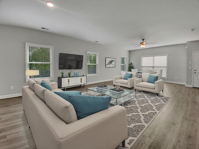 living area with baseboards, wood finished floors, visible vents, and ceiling fan