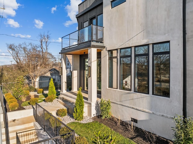 view of side of property with crawl space, a balcony, stucco siding, and fence