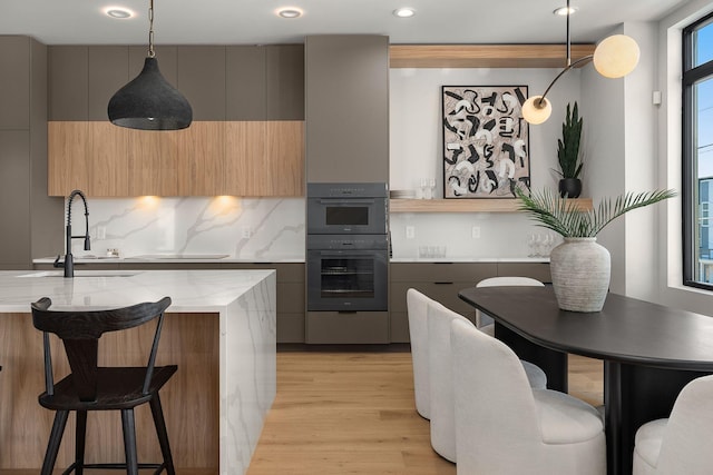 kitchen with double oven, a breakfast bar, light wood-style flooring, modern cabinets, and a sink