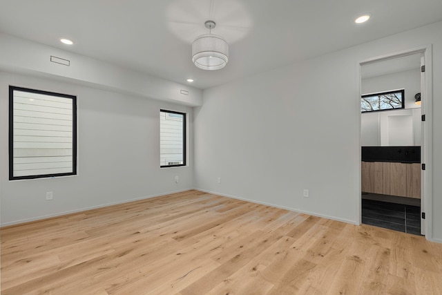 empty room featuring recessed lighting, light wood-type flooring, a wealth of natural light, and baseboards