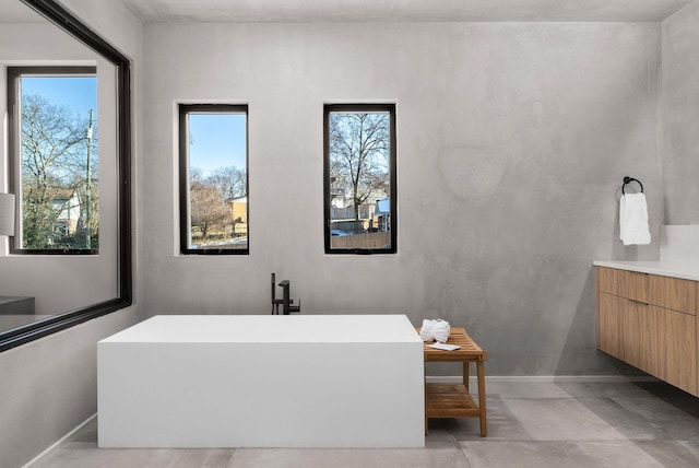 bathroom with baseboards, a soaking tub, and vanity