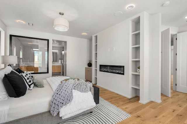 bedroom featuring light wood-type flooring, baseboards, a glass covered fireplace, and ensuite bathroom