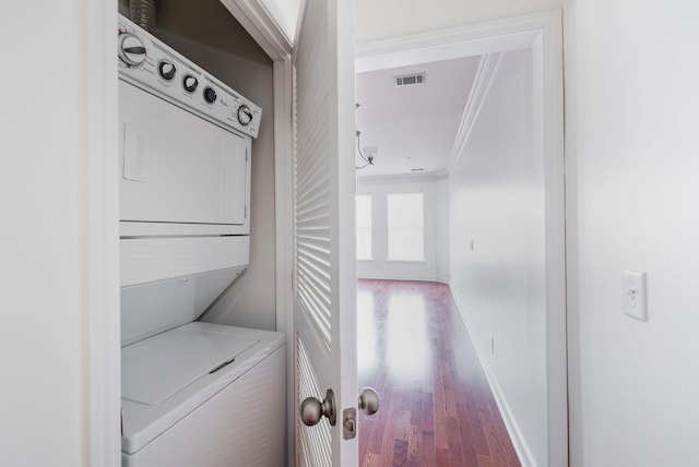 laundry area with visible vents, ornamental molding, laundry area, wood finished floors, and stacked washer / drying machine