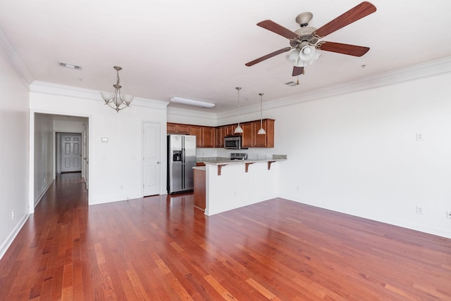 kitchen featuring visible vents, a kitchen bar, a peninsula, brown cabinetry, and stainless steel appliances