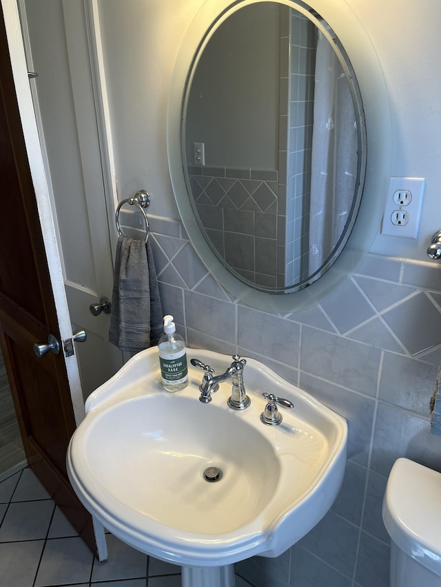 bathroom featuring tile patterned flooring, tile walls, toilet, and a sink