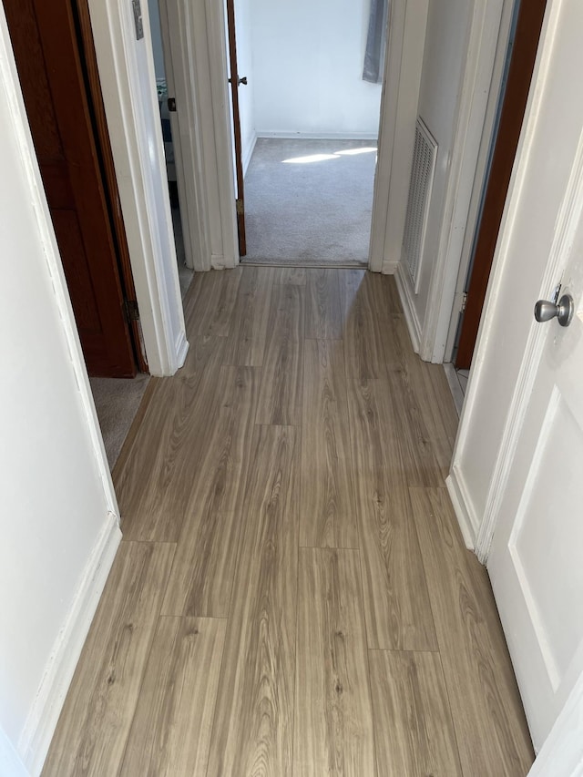 hallway featuring visible vents, baseboards, and wood finished floors