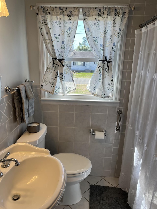 bathroom with tile patterned floors, toilet, a sink, a shower with shower curtain, and tile walls